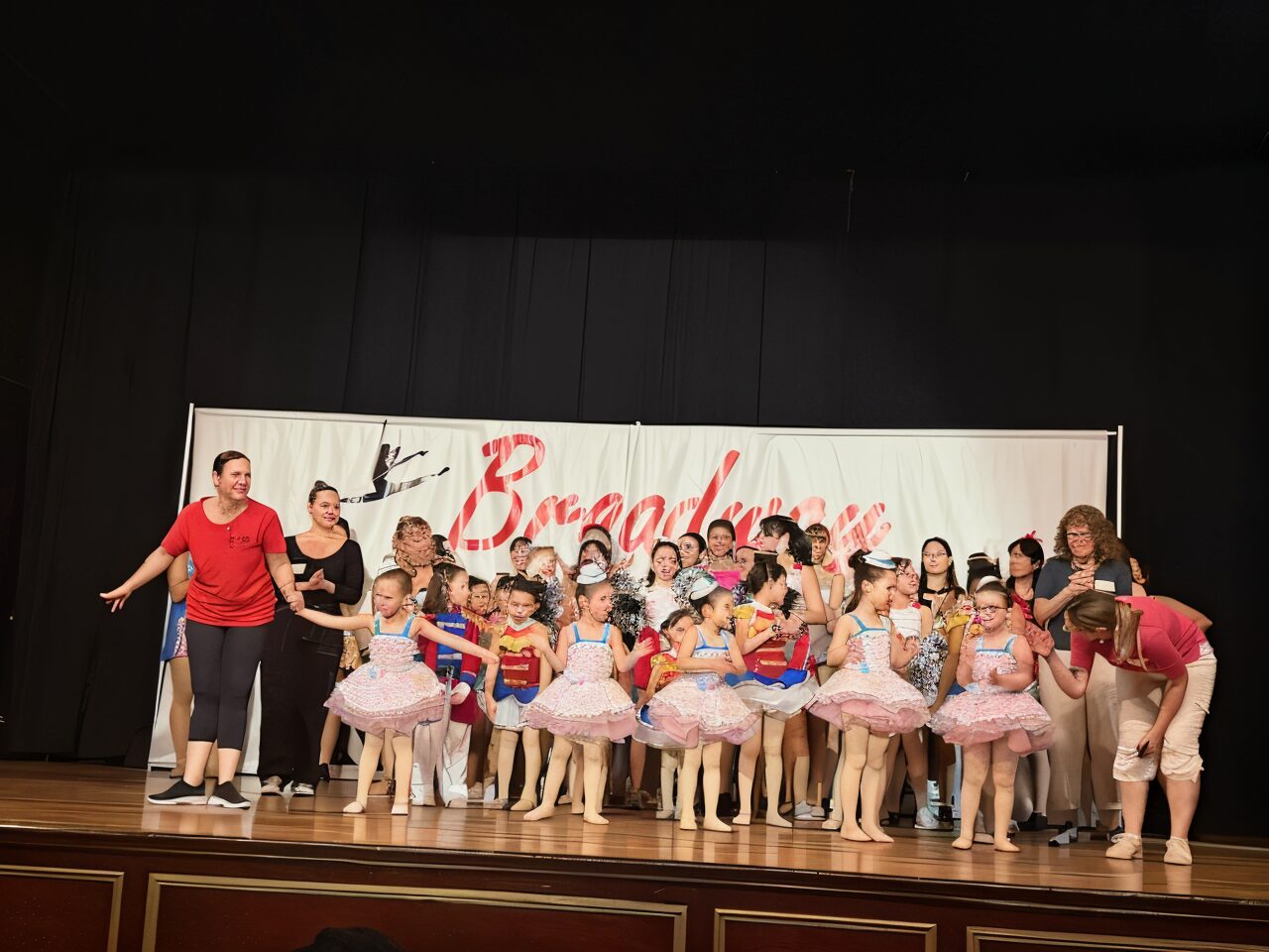 Children's ballet performance with teachers on stage.