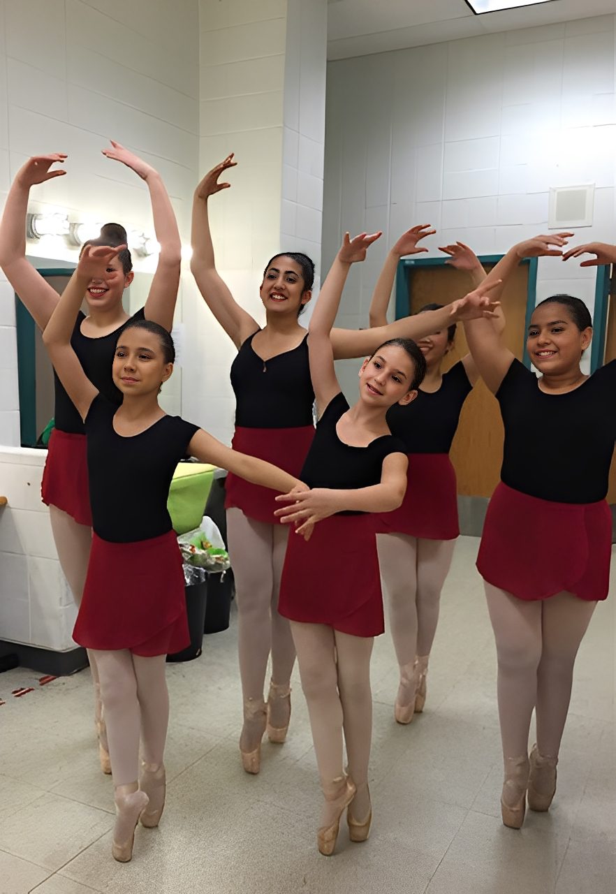 Young ballet dancers posing in a studio with red skirts and black tops.