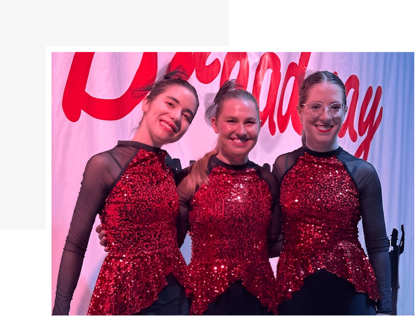 Three dancers in red sequined costumes smiling.