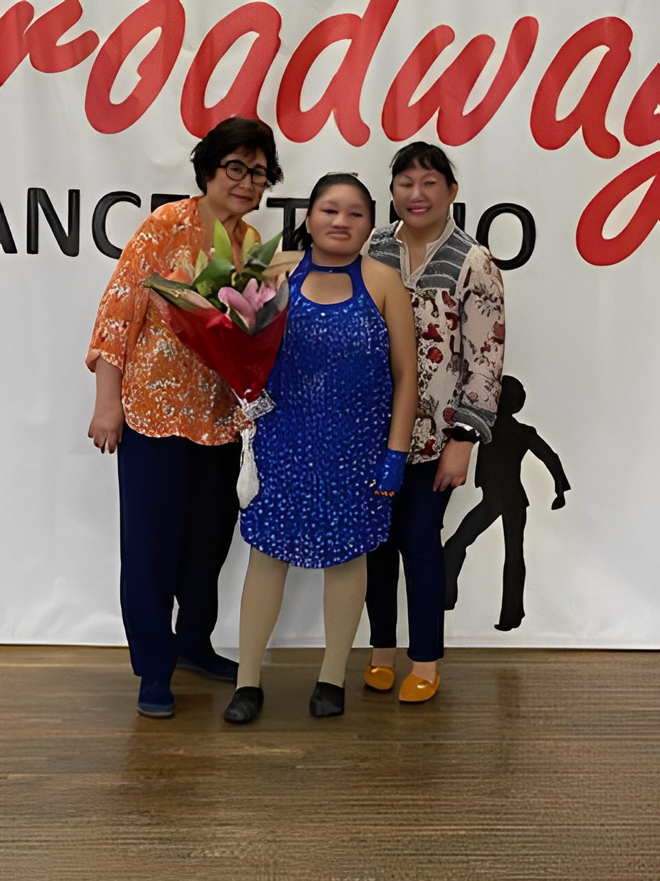 Three women posing for a photo at a dance event, one holding a bouquet.