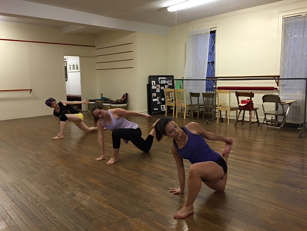 Dancers practicing floor movements in a studio with mirrors and ballet bars.