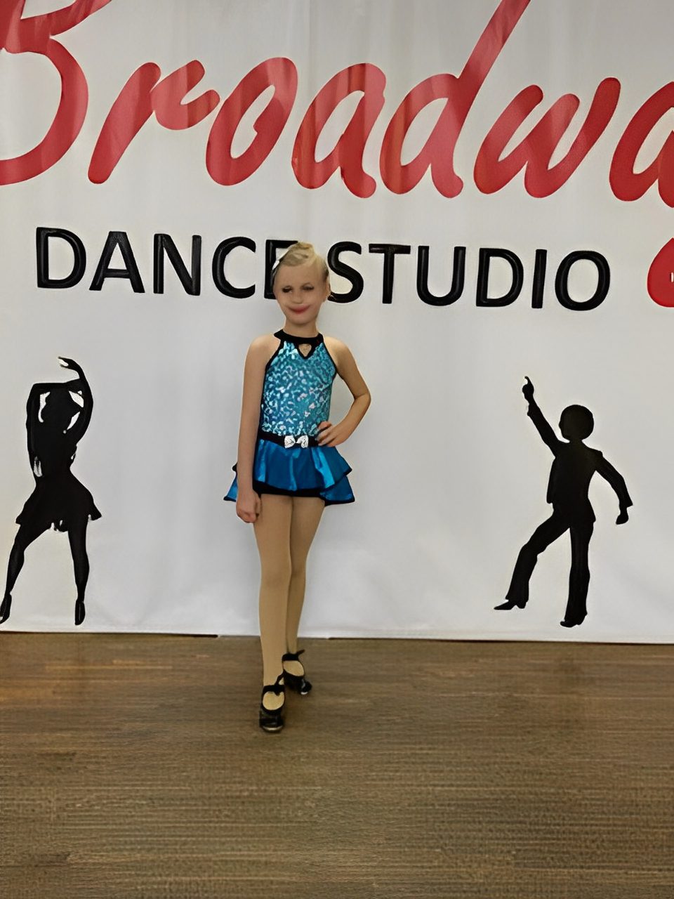 Young girl in a blue dance costume posing at a dance studio.