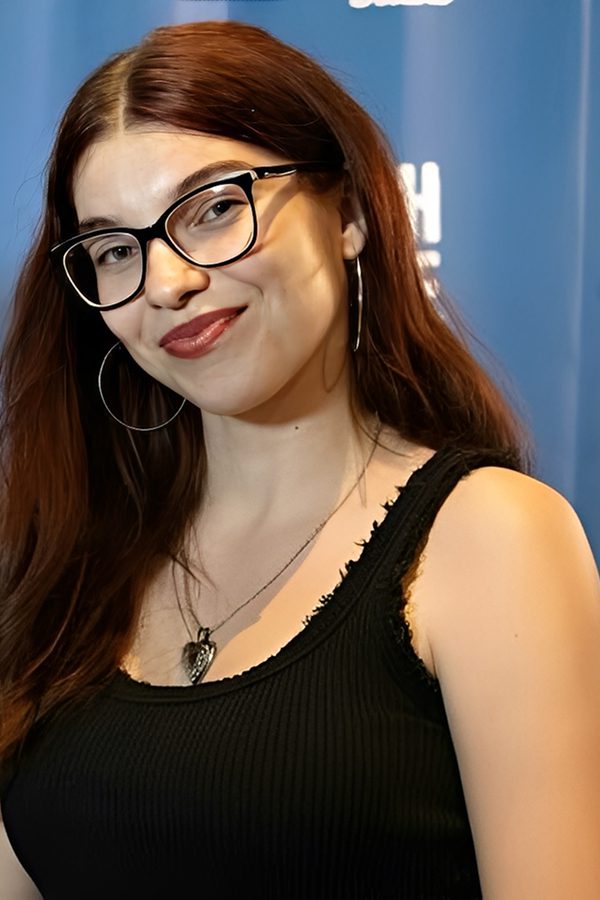 Young woman with glasses smiling, wearing a black sleeveless top.