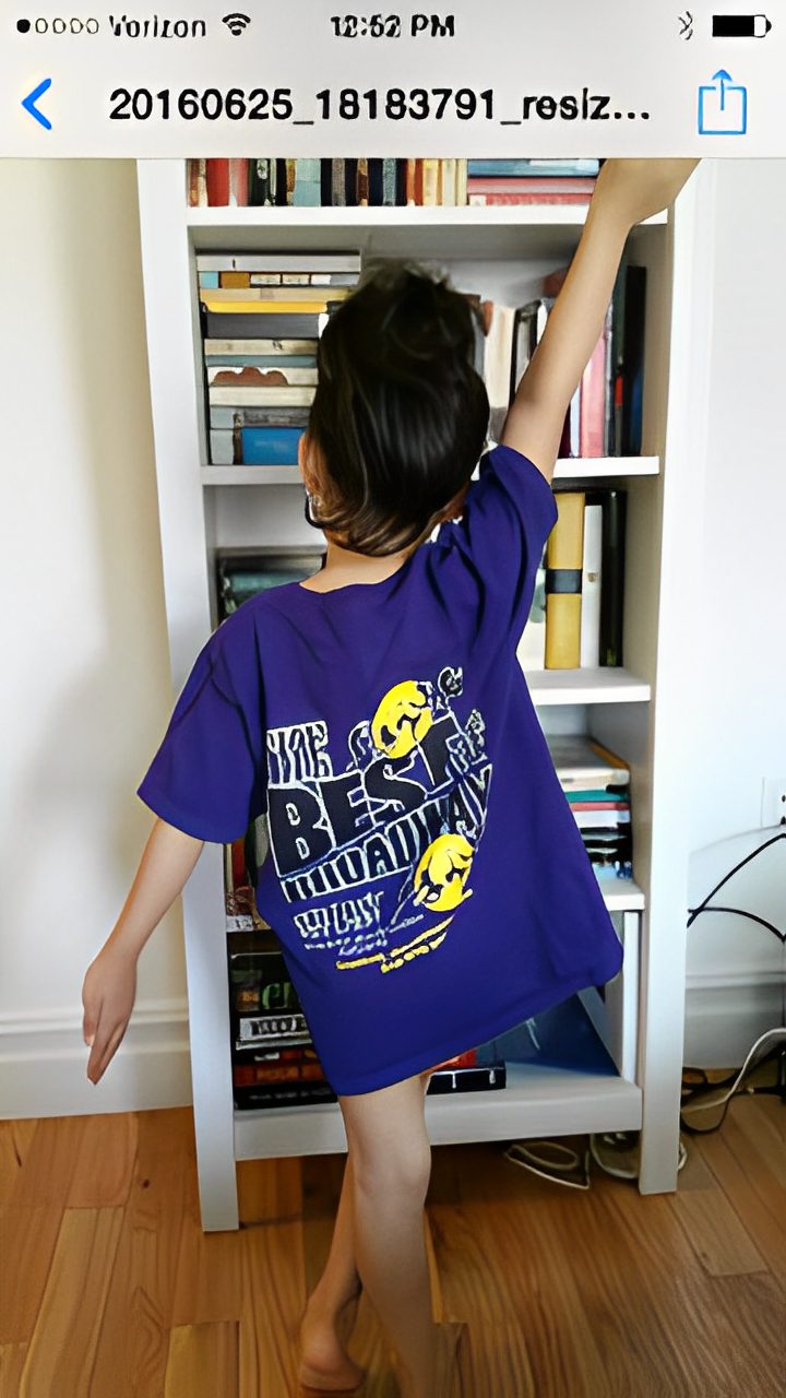 Person in a purple graphic tee with smiley faces stands in front of a bookshelf.