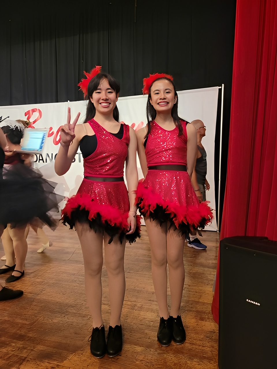 Two girls in red dance costumes posing joyfully on stage.