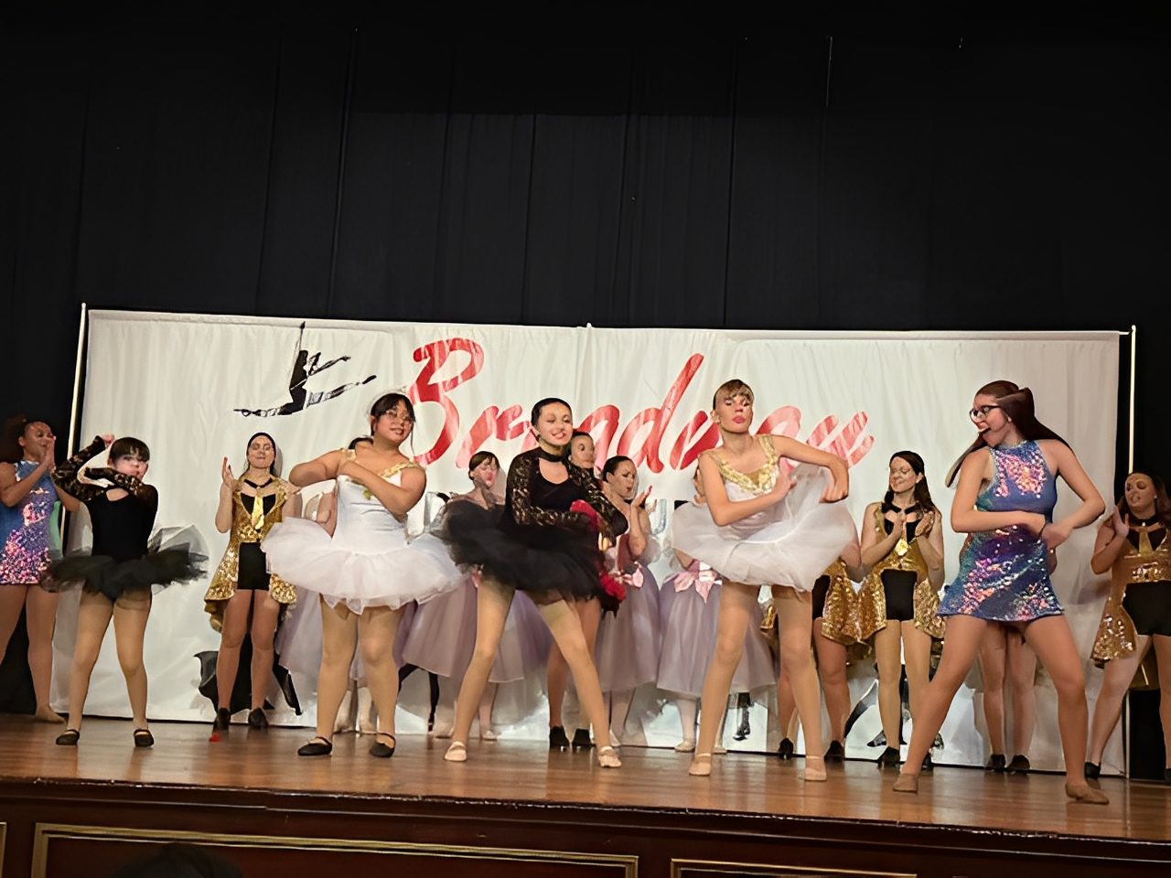 Young dancers performing ballet on stage with musicians in the background.