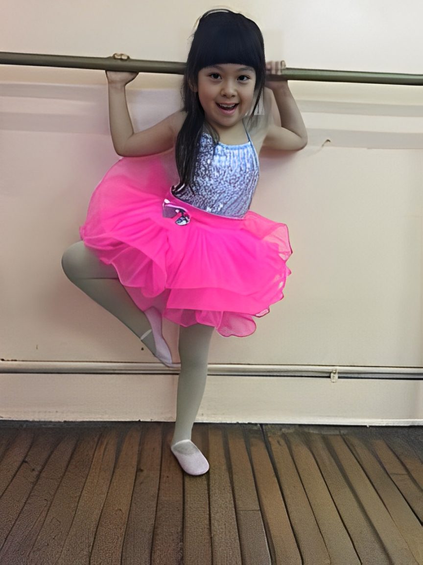 Child in pink tutu at ballet barre.